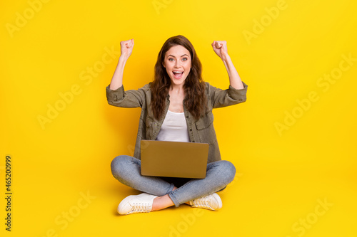 Full length portrait of pretty positive girl sit fists up open mouth achievement isolated on yellow color background © deagreez