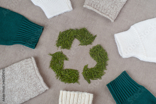  Recycle clothes concept. Used clothes. Ecological and sustainable fashion. sleeves with winter knitted sweaters. recycling sign with Christmas tree needles. High quality photo