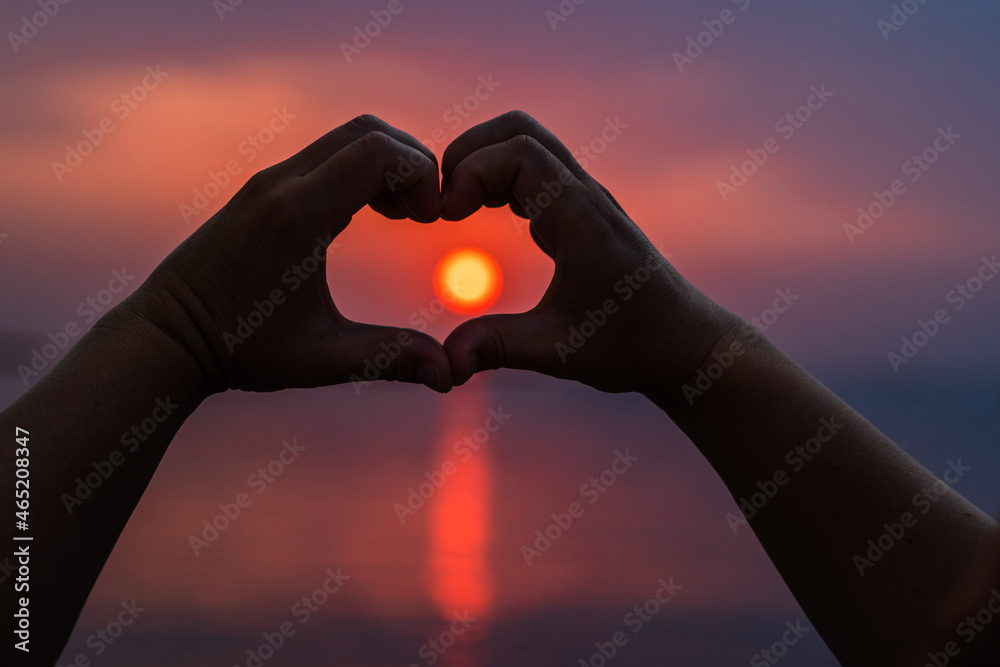 Heart shape making of hands against bright sea sunset and sunny golden way at water Heart shape making of hands against bright sea sunset and sunny golden way at water