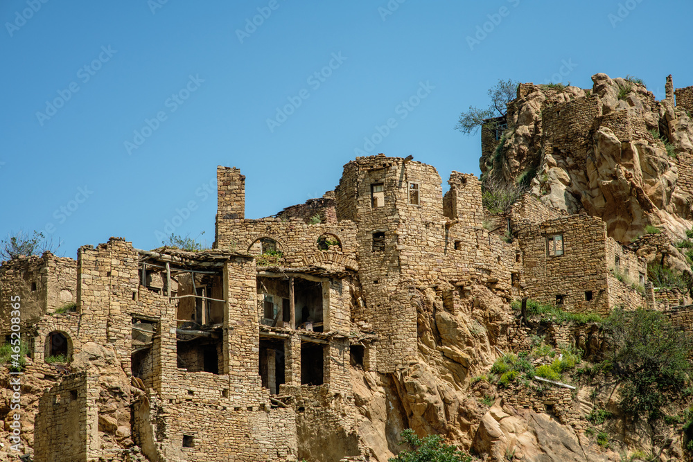 Abandoned houses of the ancient village of Gamsutl with destroyed stone walls of the building on the top of a mountain peak against the background of mountains in summer in Dagestan, Russia