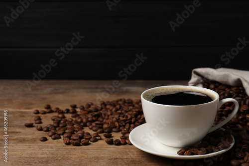 Cup of aromatic coffee and beans on wooden table. Space for text