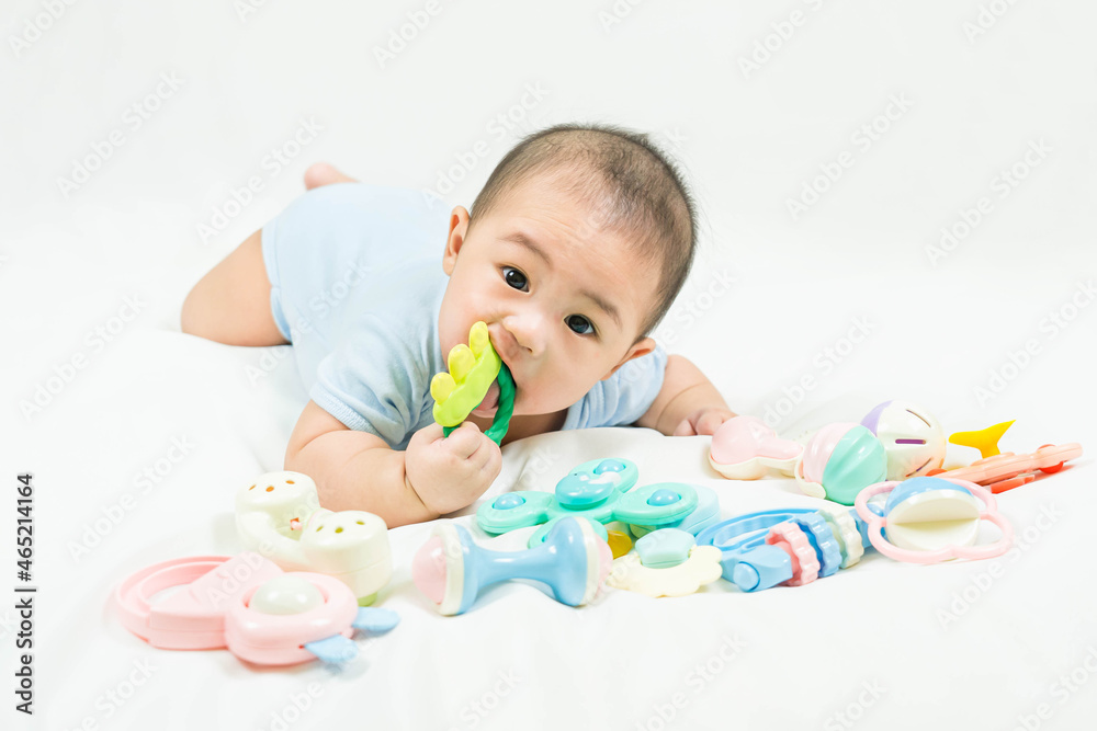 childhood and Childcare concept Portrait of cute little 5 months old asian newborn baby boy wearing blue bodysuit having teeth growing issues teething pain while holding a bite toy lying on the bed. childhood and Childcare concept Portrait of cute little 5 months old asian newborn baby boy wearing blue bodysuit having teeth growing issues teething pain while holding a bite toy lying on the bed.