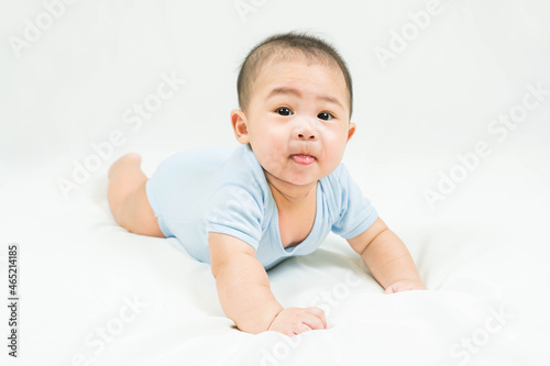 Childhood and Childcare concept Portrait of cute little 5 months old  asian newborn baby boy wearing blue bodysuit learn to crawl on white blanket at home.Smiling and looking camera.