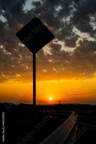 Breathtaking view of the sunset on the track. The road goes into the distance, the Shadow of the road sign. Incredibly beautiful sunset bright scarlet color and cumulus clouds in the sky.