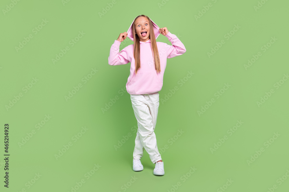 Full body photo of cheerful funky excited positive young small girl wear hoodie hands hood isolated on green color background Full body photo of cheerful funky excited positive young small girl wear hoodie hands hood isolated on green color background