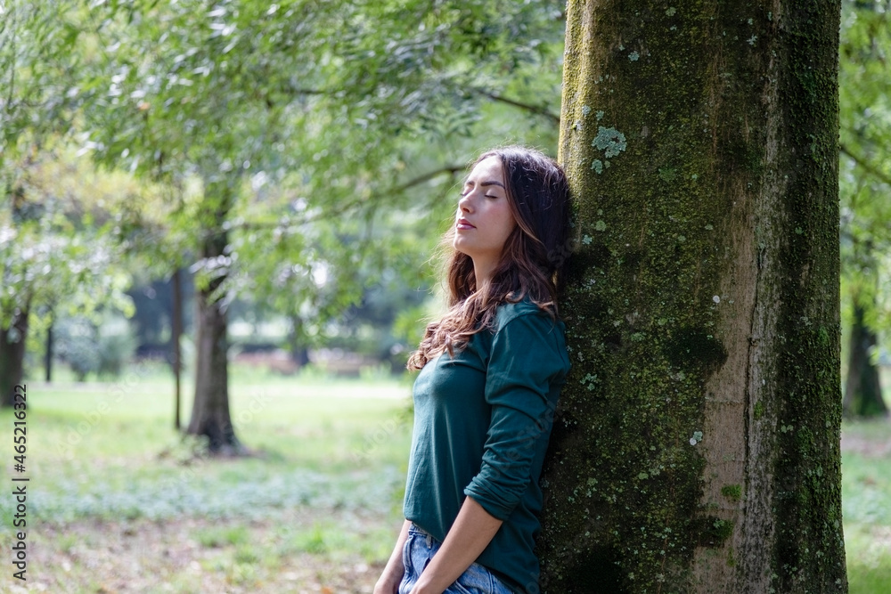 Beautiful woman with eyes closed leaning on tree trunk Beautiful woman with eyes closed leaning on tree trunk