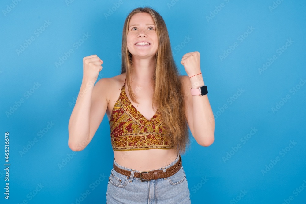 young ukranian girl wearing tank top over blue backaground champion having success being glad to achieve his goals. Victory and triumph concept. young ukranian girl wearing tank top over blue backaground champion having success being glad to achieve his goals. Victory and triumph concept.