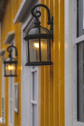 An old lamp on a yellow wooden facade with white windows
