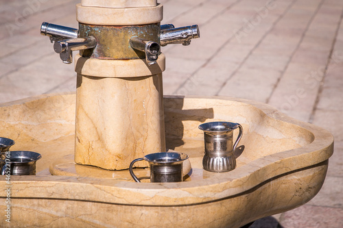 Tablou canvas Fountain with faucets and silver washing cup, jugs, for the purification or ablution ritual consisting of hand washing prior to prayer
