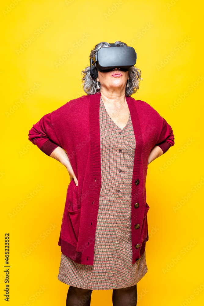 Senior woman with hand on hip wearing virtual reality headset while standing against yellow background