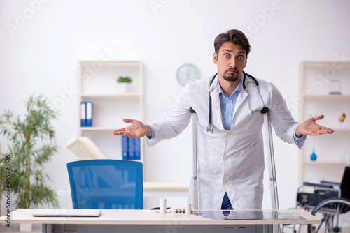 Young male doctor with crutches working in the clinic