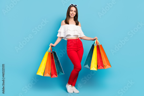 Full size photo of nice brunette lady hold bags wear spectacles white top jeans isolated on blue color background