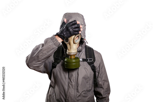 An isolated shot of a man dressed in a gas mask, a jacket with a hood, a backpack, put his hand on his head from grief and trouble. On a white isolated background