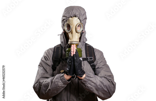 An isolated shot of a man dressed in a gas mask, a jacket with a hood, a backpack, praying, pressed the palms of his hands against each other. On a white isolated background