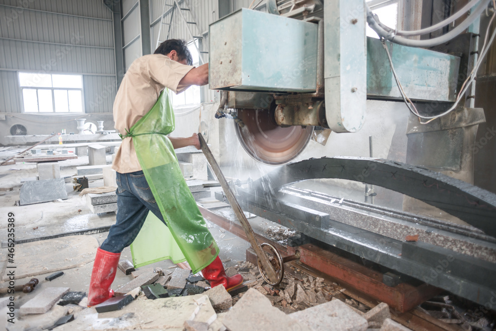 Worker operating a industrial machine for cutting stone in a Chinese factory Worker operating a industrial machine for cutting stone in a Chinese factory