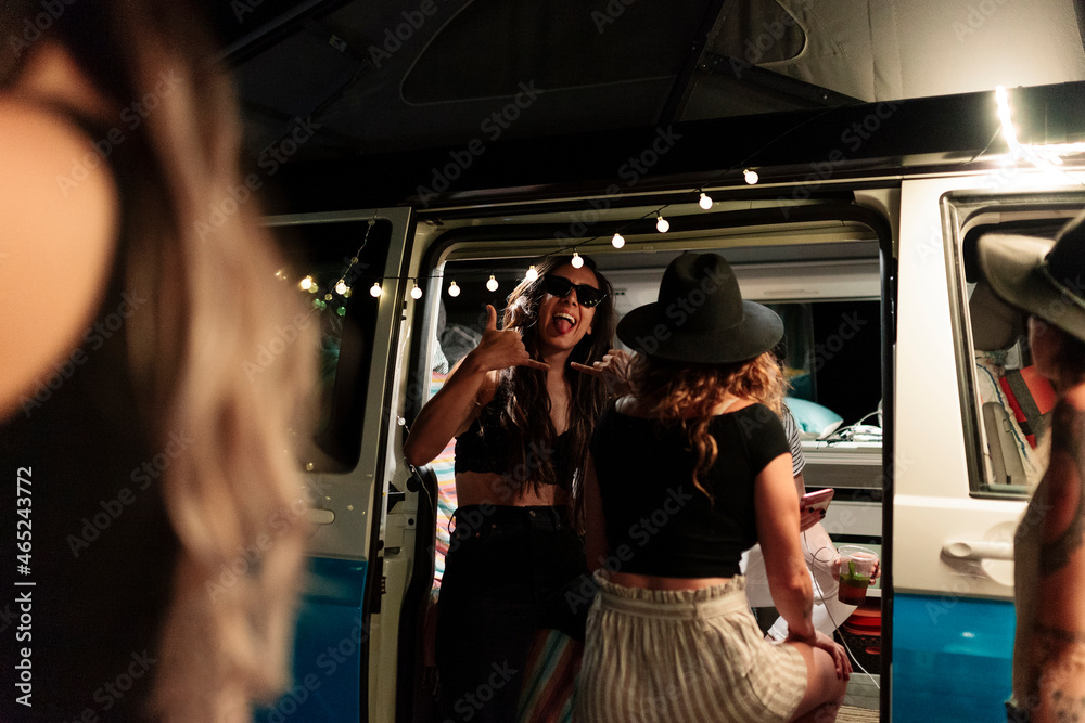 Woman showing shaka sign during party with female friends in camper van Woman showing shaka sign during party with female friends in camper van