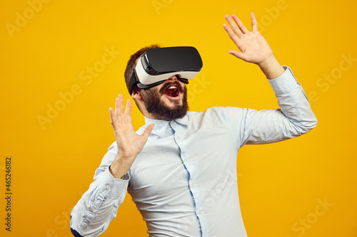 Excited young male wearing virtual reality helmet touching the air  isolated over yellow background. Horizontal studio shot.