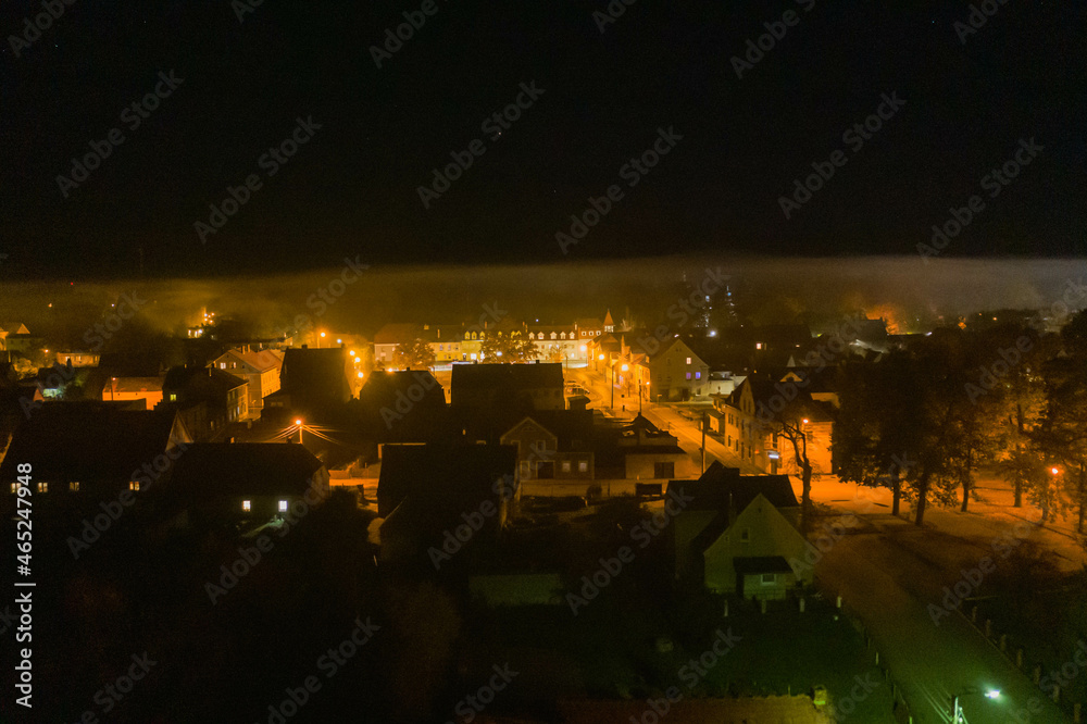 Fototapeta premium Panorama małego miasteczka Iłowa położonego w Polsce. Jest noc. Ciemności rozświetla światło latarni. Widok z drona.
