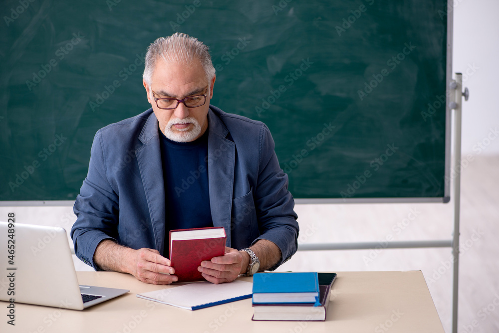 Old male teacher holding book in the classroom Old male teacher holding book in the classroom