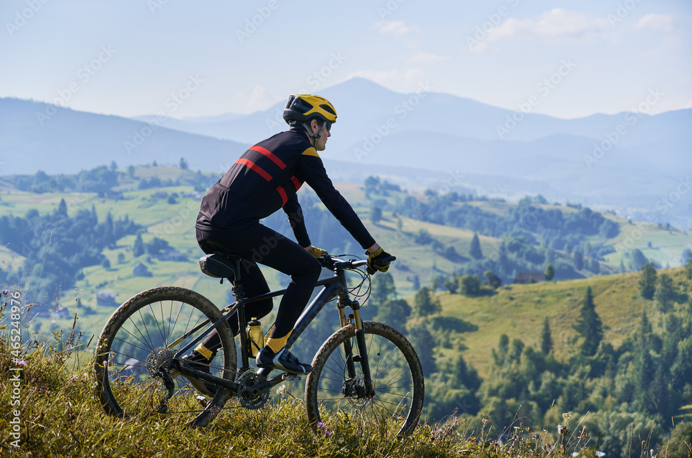 Man riding his bicycle in the mountains in early foggy morning going downhill. Peaks in clouds, green hills on background. Side view. Concept of active lifestyle
