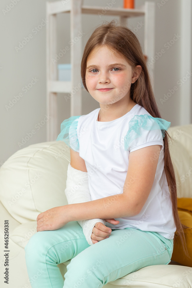 Child with a cast on a broken wrist or arm smiling and having fun on a couch. Positive attitude, recovery and kid concept. Child with a cast on a broken wrist or arm smiling and having fun on a couch. Positive attitude, recovery and kid concept.