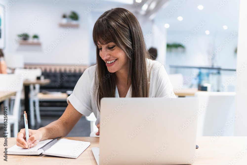 Smiling female professional with laptop writing in diary at table