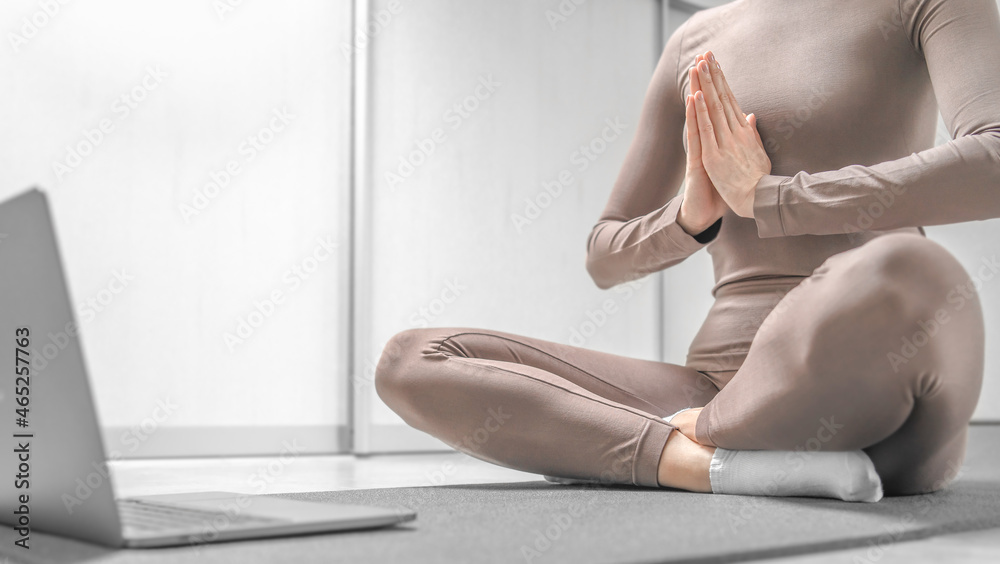 Photo of woman practicing yoga training online at home with laptop.