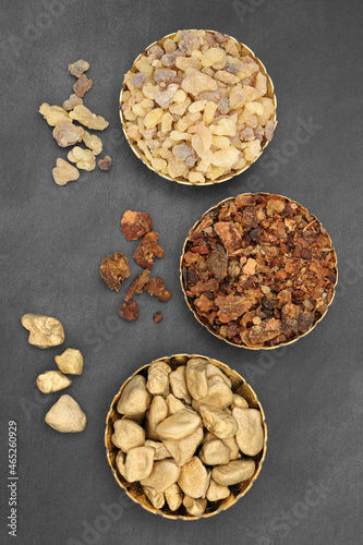 Gold frankincense and myrrh composition in bowls and loose. Christian religious symbols given to Jesus Christ at his birth by the Three Wise Men. Top view on mottled grey background. photo