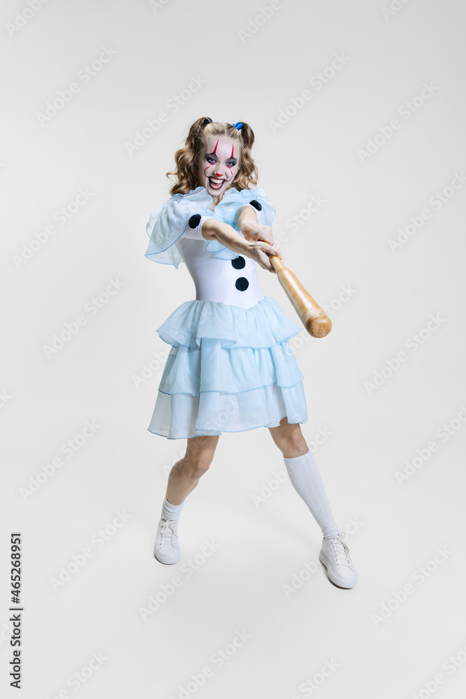 Halloween spooky theme. Portrait of beautiful artistic girl in halloween make-up and costume of dancing clown isolated over grey background
