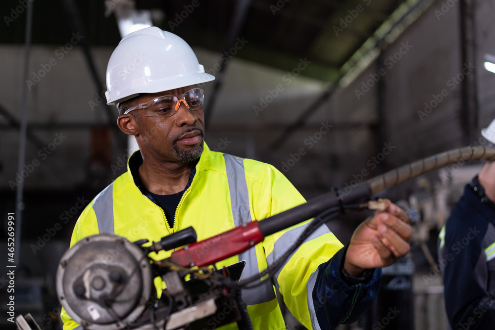 Male engineer worker maintenance the automatic robotic machine in the factory. Black male technician worker working with control automatic robot arm system welding Male engineer worker maintenance the automatic robotic machine in the factory. Black male technician worker working with control automatic robot arm system welding