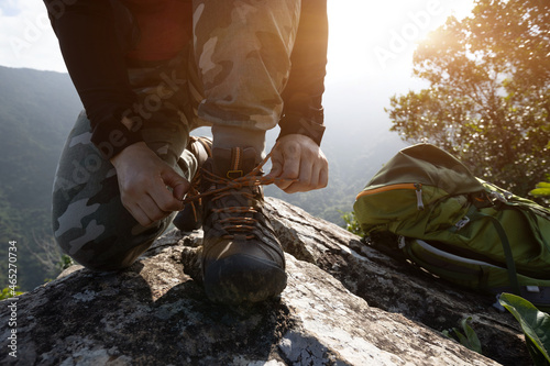 Successful hiker tying shoelace on mountain top cliff edge