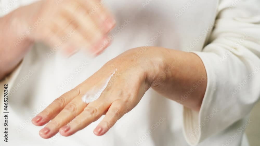 Old woman applying hand cream close-up. Using anti-wrinkle moisturizing serum, beauty procedure, morning routine in bathroom. Cosmetology and skin care concept, cosmetic products. Old woman applying hand cream close-up. Using anti-wrinkle moisturizing serum, beauty procedure, morning routine in bathroom. Cosmetology and skin care concept, cosmetic products.