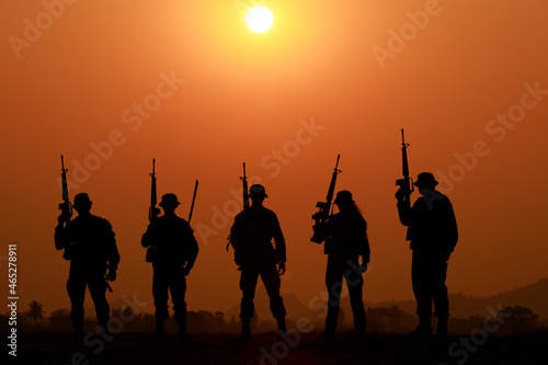 Silhouette of military soldier or officer with weapons at sunset. shot, holding gun, standing in a row colorful sky, background