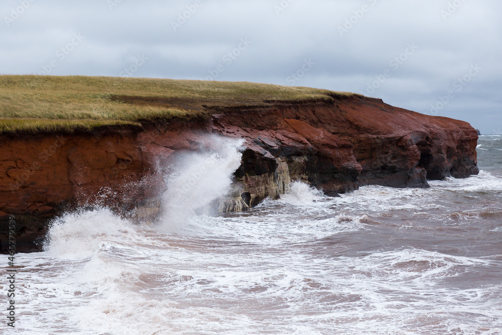 Waves crashing on red sandstone cliffs seen in L’Étang-du-Nord village during a stormy fall day, Cap-aux-Meules island, Magdalen Islands, Quebec, Canada Waves crashing on red sandstone cliffs seen in L’Étang-du-Nord village during a stormy fall day, Cap-aux-Meules island, Magdalen Islands, Quebec, Canada