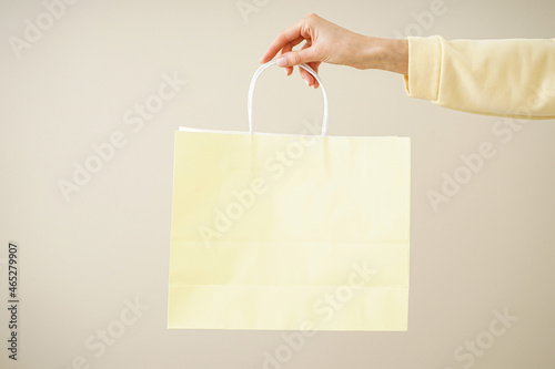 Paper yellow bag, eco packaging in a female hand on a beige background, space for text.