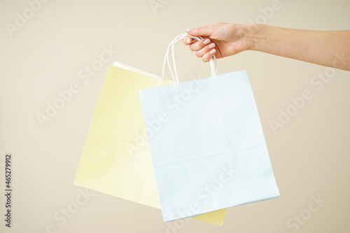 Paper yellow and blue bag in a female hand on a beige background. Space for text.