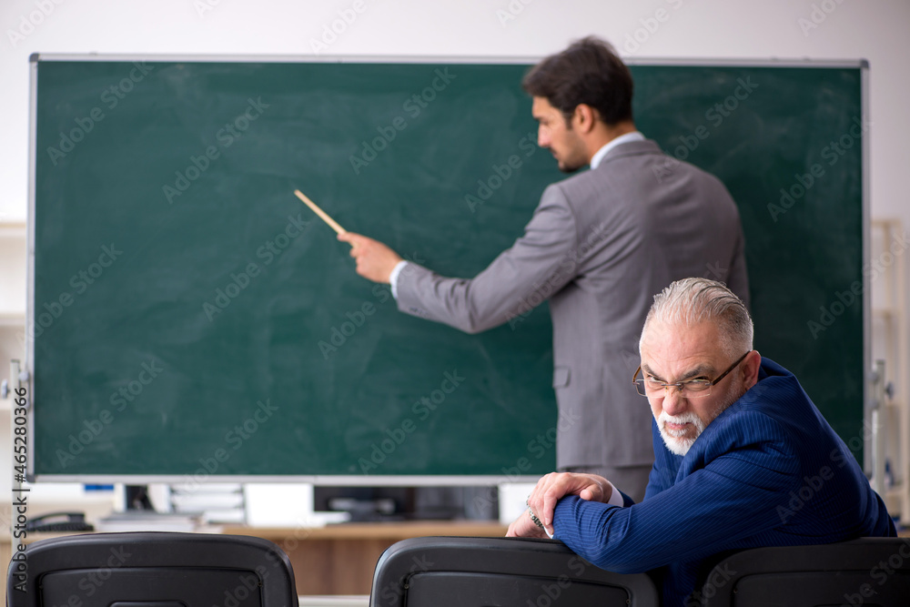 Young male employee and old boss in front of blackboard Young male employee and old boss in front of blackboard