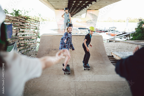 Friends skateboarders doing tricks while rolling on half pipe in skate park. Sport, children and outdoor activities in extreme park. Happy kids on skateboards at ramp. Young skateboarders in skatepark photo