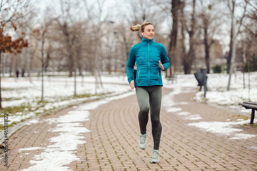 Fit sportswoman running on path in park on snowy winter day. Recreation, snowy weather, winter day © dusanpetkovic1