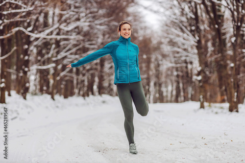 Fit sportswoman standing in snow in forest and doing fitness exercises. Healthy life, winter fitness