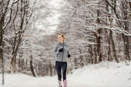 Sportswoman running in woods at snowy winter day. Winter sport, outdoor fitness, healthy life