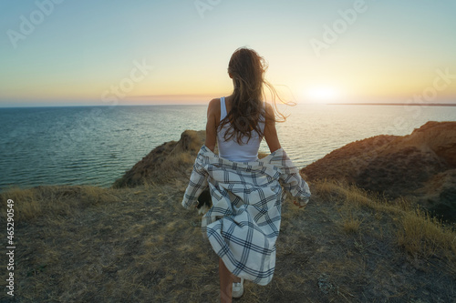 Obraz na plátně Back view brunette blowing hair woman walking by hill top with the panoramic view at sunset