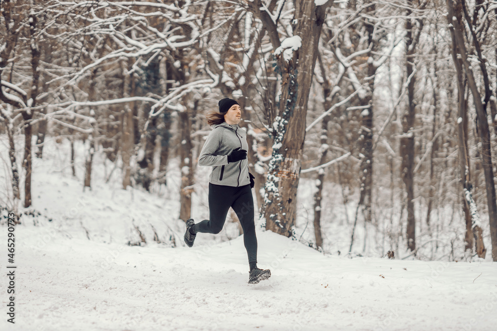 Fit runner running in woods on the snow at winter. Outdoor fitness, winter sport, cardio exercises