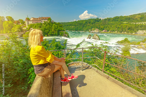 Elegant girl sitting on the panoramic view over the in the Rhine Falls in Switzerland. Swiss biggest waterfall of Europe. 490 ft wide and 75 ft high. Schaffhausen and Zurich cantons. photo