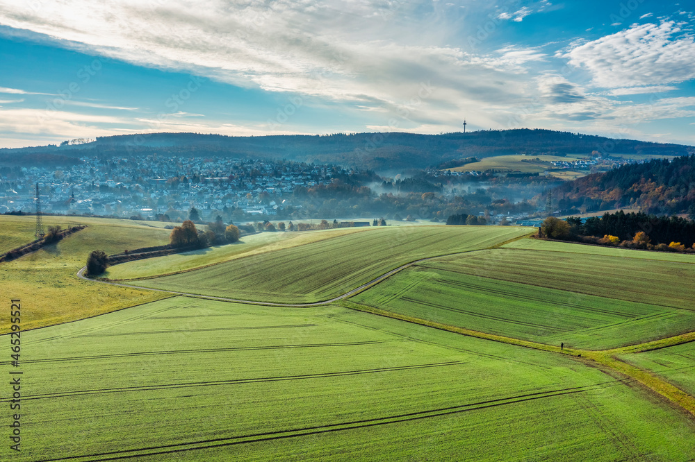 View of a slightly hilly landscape in the Taunus with light morning fog over the city in the background