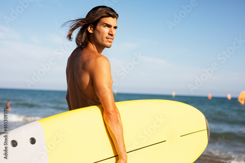 Portrait of handsome surfer with his surfboard. Young man with a surfboard on the beach... photo