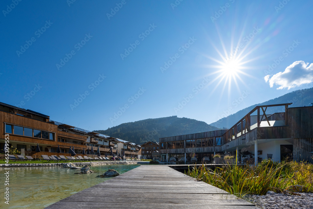 Outside area at holiday resort with modern pool house with old wood construction and sunbeams in the blue sky
