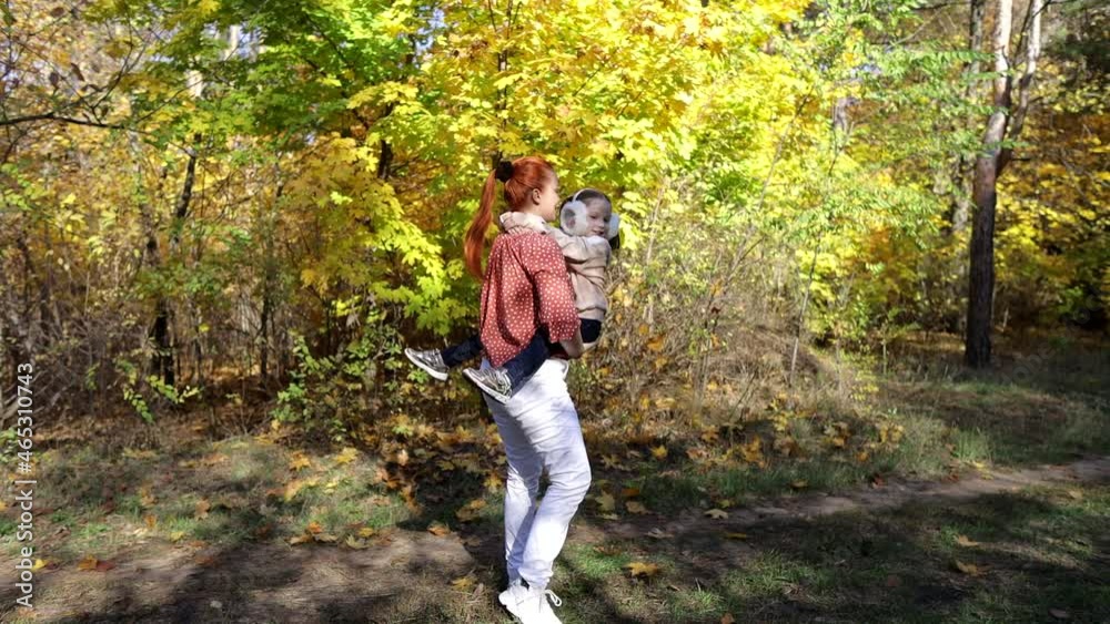 a red-haired happy woman with a little daughter in her arms in an autumn sunny park a red-haired happy woman with a little daughter in her arms in an autumn sunny park