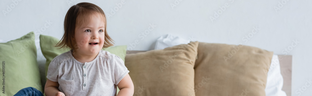 Smiling toddler girl with down syndrome looking away on bed, banner. Smiling toddler girl with down syndrome looking away on bed, banner.