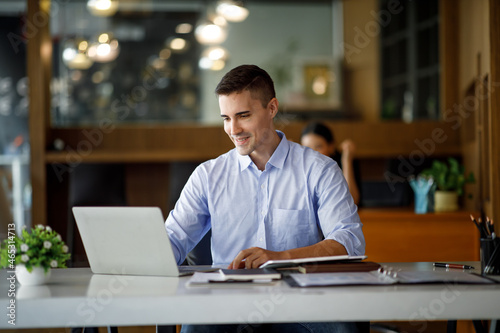 Foto Smiling businessman working on a laptop computer in a modern office,doing finances, accounting analysis, report data pointing graph Freelance education and technology concept